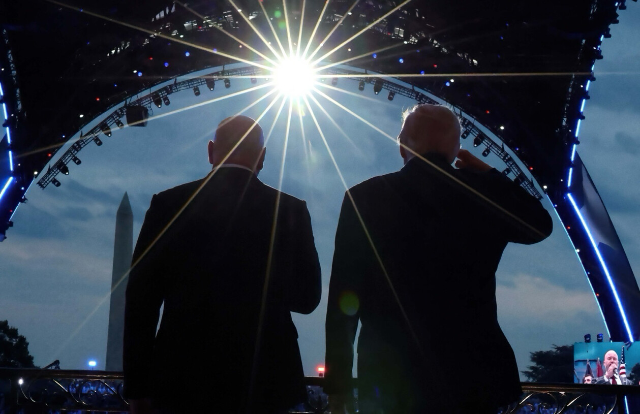 Two men in dark suits stand silhouetted on a stage overlooking the National Mall in Washington, D.C. on 07/05/2026.