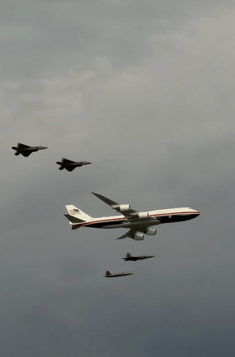 The new Air Force One flies in formation with four F-22 Raptors over an undisclosed location on 07/04/2026. The aircraft features a redesigned red, white, and dark blue livery, which was proposed during the Trump administration, departing from the traditional light blue and white design.